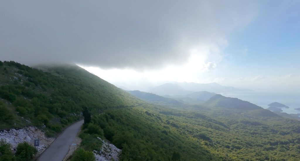 Essential Camera Gear for Motorcycle Travel Photography Aerial drone shot above Montenegro mountain road with Shkodra Lake visible — DJI Neo motorcycle travel photography