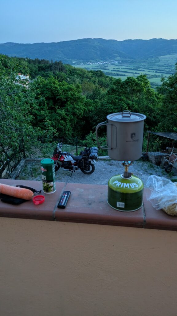 Compact camping stove cooking simple meal at motorcycle campsite showing maximum savings food strategy for budget touring 