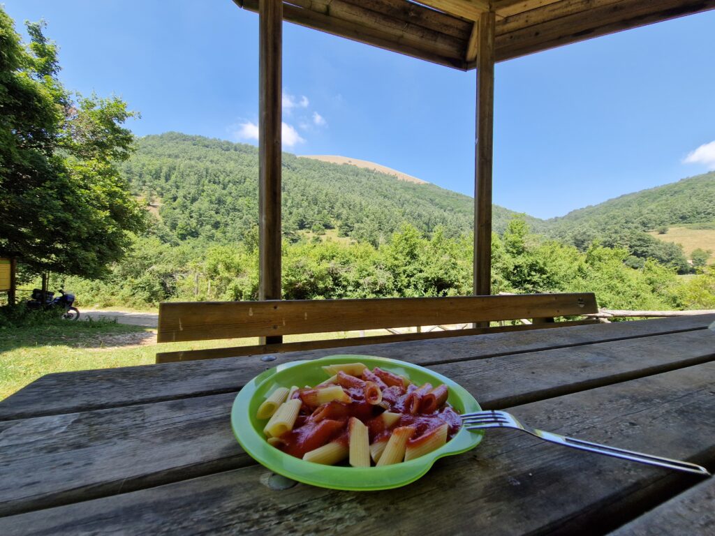 Motorcycle tourer eating simple outdoor lunch with bread cheese and local produce showing cheap food motorcycle touring approach