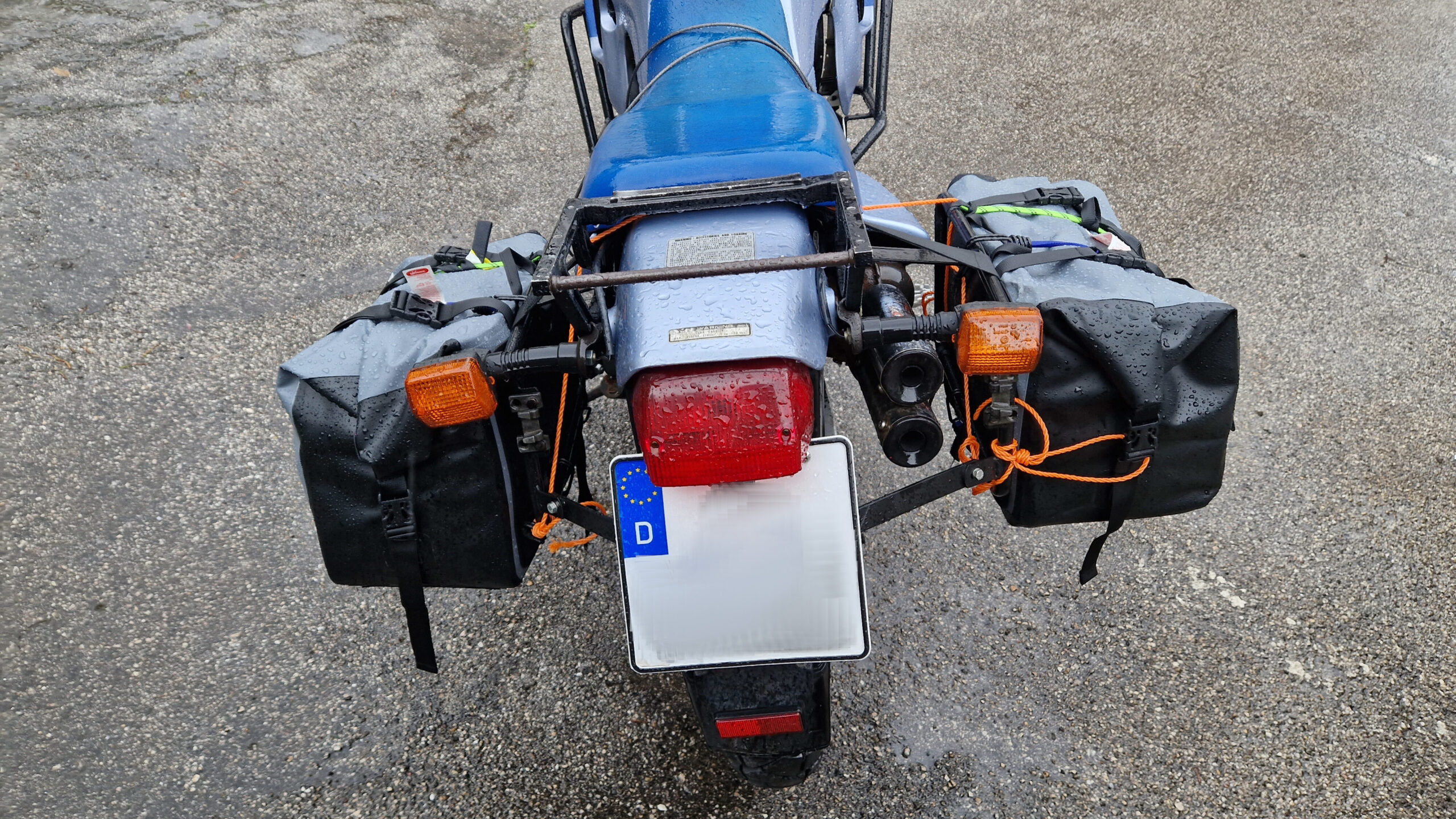 Motorcycle soft luggage attached with straps showing routing around subframe and anti-slip matting underneath for secure soft luggage mounting